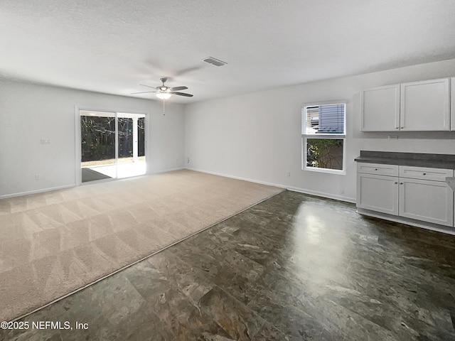 unfurnished living room featuring ceiling fan, a textured ceiling, and dark carpet