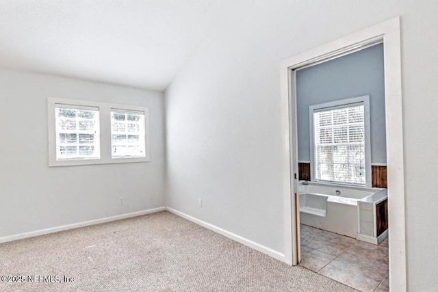 unfurnished bedroom featuring light carpet, vaulted ceiling, and baseboards