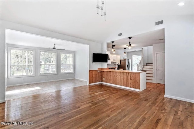 kitchen featuring lofted ceiling, visible vents, wood finished floors, a peninsula, and stainless steel fridge with ice dispenser