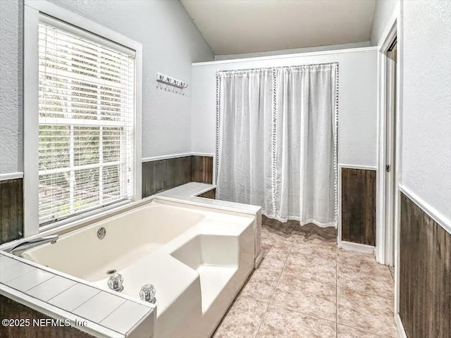 full bath featuring tile patterned flooring, wainscoting, a garden tub, and a textured wall