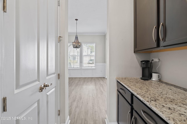 kitchen featuring crown molding, decorative light fixtures, light stone countertops, and light hardwood / wood-style flooring