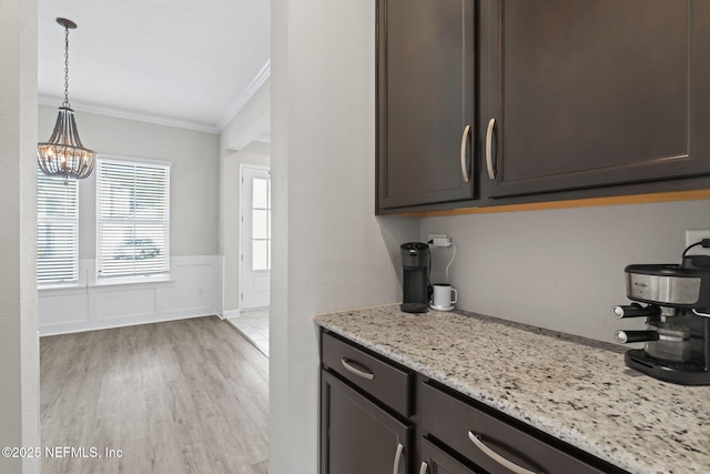 kitchen with dark brown cabinetry, crown molding, hanging light fixtures, light stone countertops, and light hardwood / wood-style floors