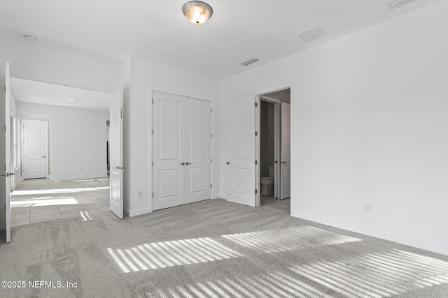 unfurnished bedroom with light carpet, ensuite bath, and a closet