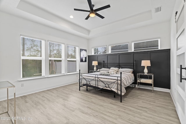 bedroom featuring a raised ceiling, ceiling fan, and light wood-type flooring