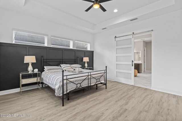 bedroom featuring ceiling fan, hardwood / wood-style flooring, a barn door, and a raised ceiling