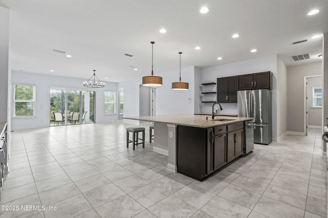 kitchen with sink, light stone counters, decorative light fixtures, a center island with sink, and appliances with stainless steel finishes