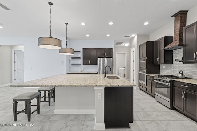 kitchen with stainless steel appliances, decorative light fixtures, a kitchen breakfast bar, and an island with sink