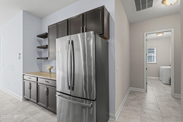 kitchen with dark brown cabinetry, light stone countertops, a textured ceiling, and stainless steel refrigerator