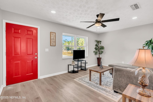 living room with ceiling fan, a textured ceiling, and light wood-type flooring