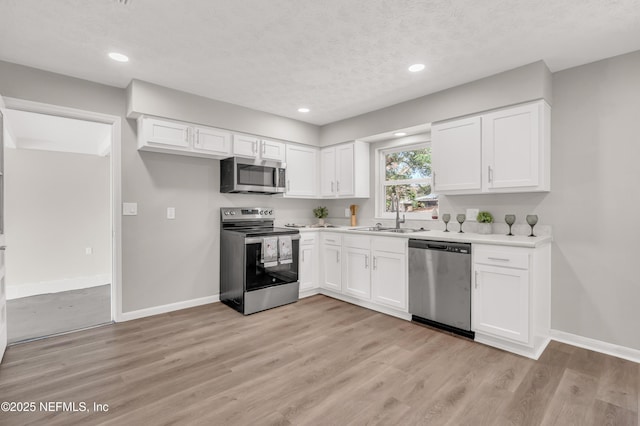 kitchen with sink, light hardwood / wood-style flooring, appliances with stainless steel finishes, white cabinetry, and a textured ceiling