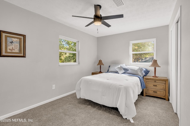 bedroom with multiple windows, ceiling fan, light colored carpet, and a textured ceiling