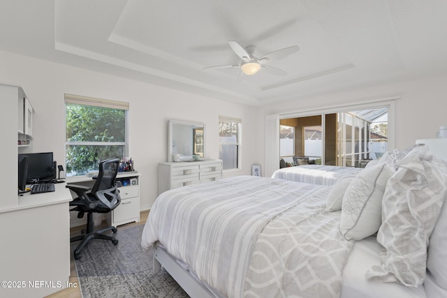 bedroom featuring ceiling fan, access to exterior, a raised ceiling, and hardwood / wood-style floors