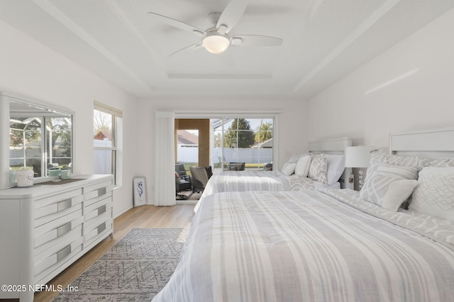 bedroom with a raised ceiling, ceiling fan, access to exterior, and light wood-type flooring