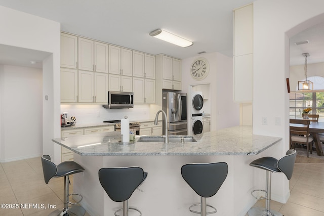 kitchen with stacked washer / drying machine, stainless steel appliances, a kitchen breakfast bar, and sink