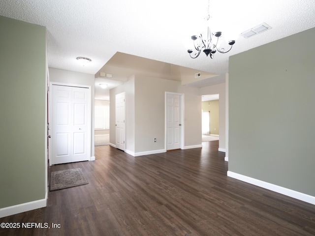 empty room featuring dark hardwood / wood-style flooring, an inviting chandelier, and a textured ceiling