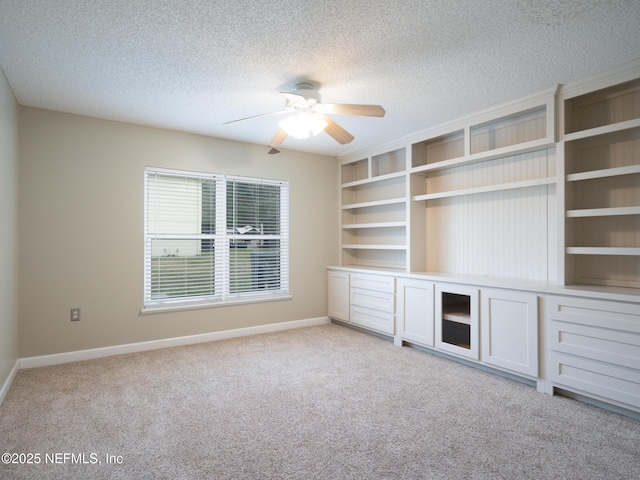 unfurnished living room featuring ceiling fan, light colored carpet, built in features, and a textured ceiling