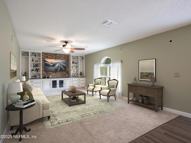 living room with built in shelves, ceiling fan, wood-type flooring, and a textured ceiling