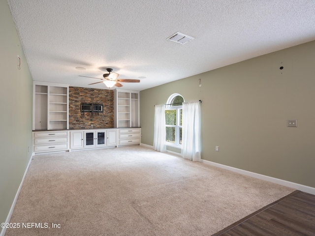 unfurnished living room featuring built in shelves, ceiling fan, carpet floors, and a textured ceiling