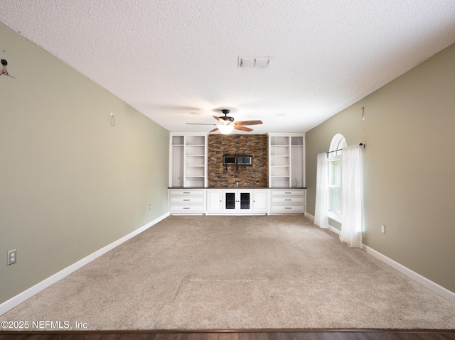 unfurnished living room with built in shelves, ceiling fan, carpet floors, and a textured ceiling