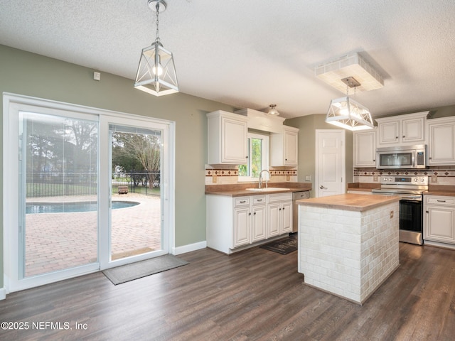 kitchen with appliances with stainless steel finishes, white cabinetry, butcher block counters, a center island, and decorative light fixtures