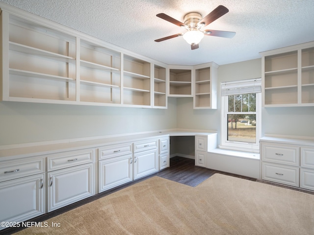 unfurnished office with ceiling fan, built in desk, and a textured ceiling