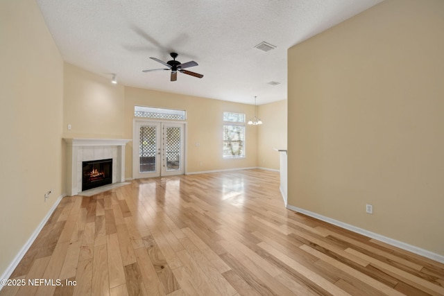 unfurnished living room featuring a tile fireplace, light hardwood / wood-style floors, a textured ceiling, ceiling fan with notable chandelier, and french doors