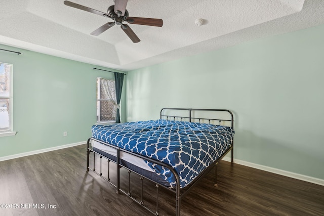 bedroom with dark hardwood / wood-style flooring, ceiling fan, a raised ceiling, and a textured ceiling