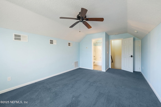 interior space featuring ceiling fan, dark carpet, vaulted ceiling, and a textured ceiling