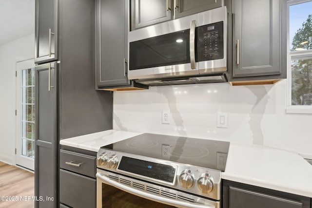 kitchen with light hardwood / wood-style flooring, stainless steel appliances, gray cabinetry, and light stone countertops