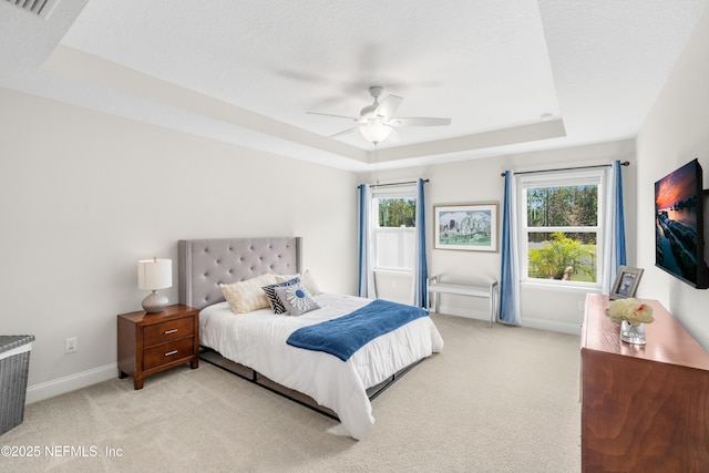 bedroom with light colored carpet, ceiling fan, and a tray ceiling