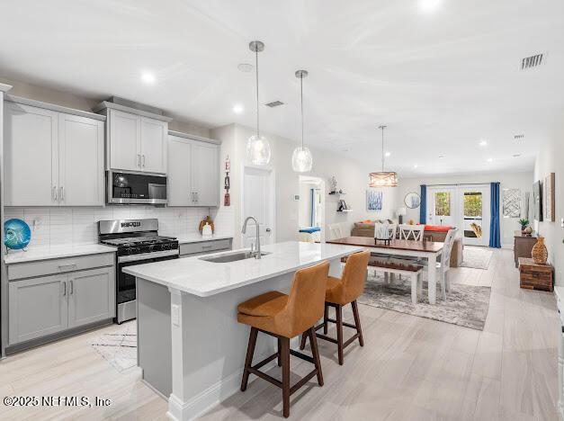 kitchen with sink, a breakfast bar area, a center island with sink, pendant lighting, and stainless steel appliances