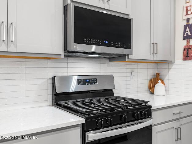 kitchen with backsplash, light stone countertops, gas range oven, and white cabinets