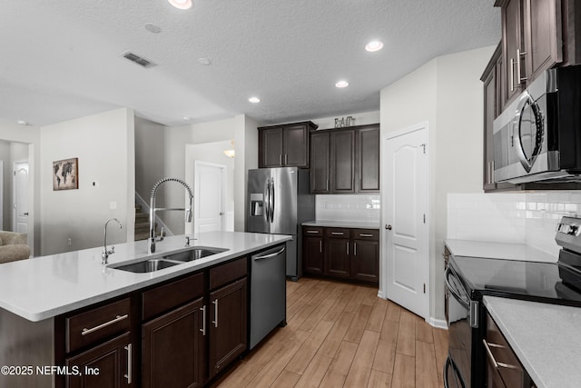 kitchen featuring sink, an island with sink, stainless steel appliances, light hardwood / wood-style floors, and decorative backsplash