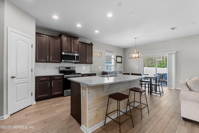 kitchen featuring sink, a breakfast bar, appliances with stainless steel finishes, a kitchen island with sink, and hanging light fixtures