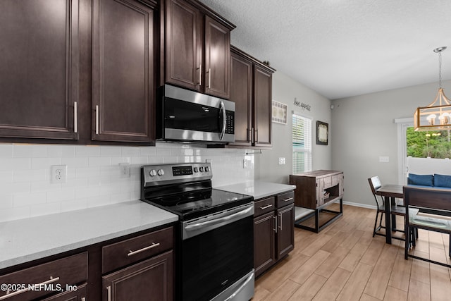 kitchen with appliances with stainless steel finishes, backsplash, hanging light fixtures, dark brown cabinets, and light hardwood / wood-style flooring