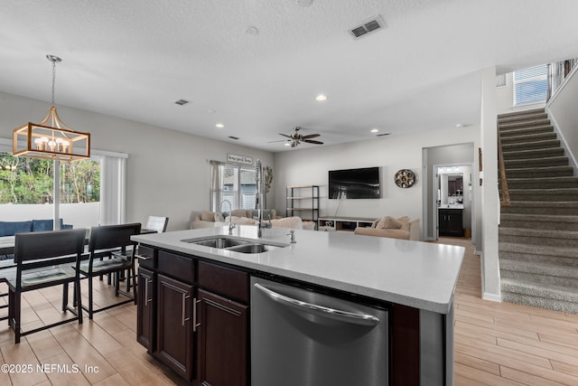 kitchen with pendant lighting, stainless steel dishwasher, a kitchen island with sink, and light hardwood / wood-style flooring