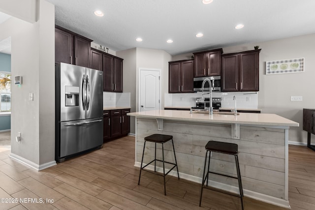 kitchen featuring appliances with stainless steel finishes, a kitchen breakfast bar, tasteful backsplash, light hardwood / wood-style floors, and a center island with sink