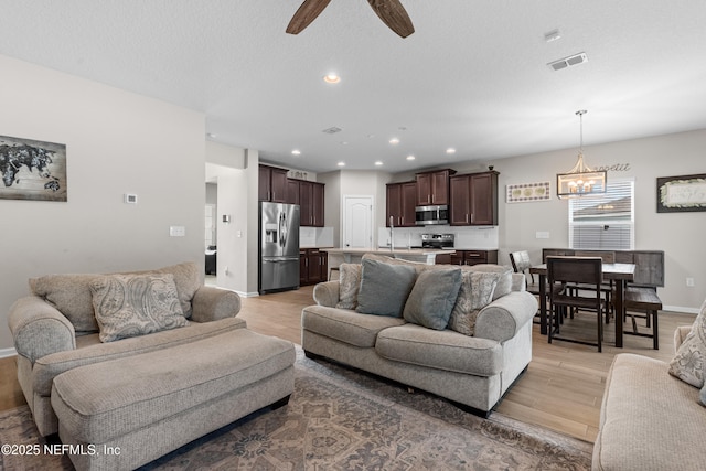 living room featuring ceiling fan with notable chandelier, light hardwood / wood-style floors, and a textured ceiling