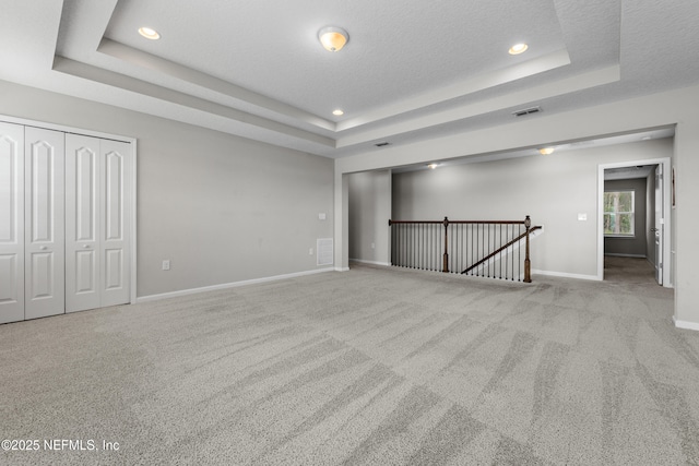 carpeted empty room with a raised ceiling and a textured ceiling