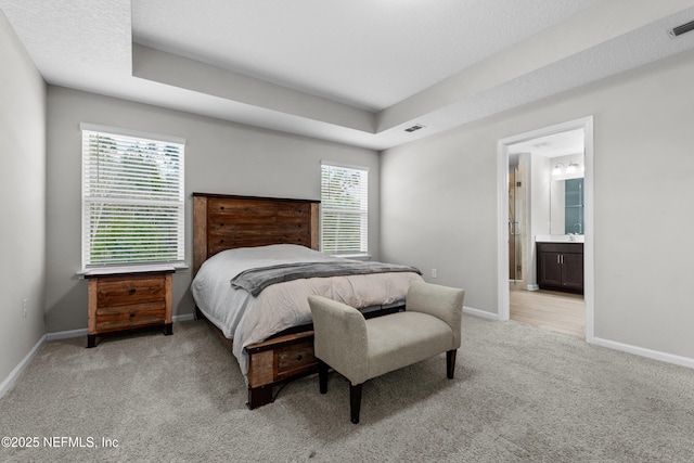 carpeted bedroom featuring a raised ceiling, ensuite bathroom, and a textured ceiling