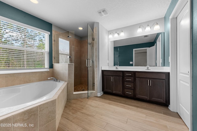 bathroom with wood-type flooring, shower with separate bathtub, vanity, and a textured ceiling