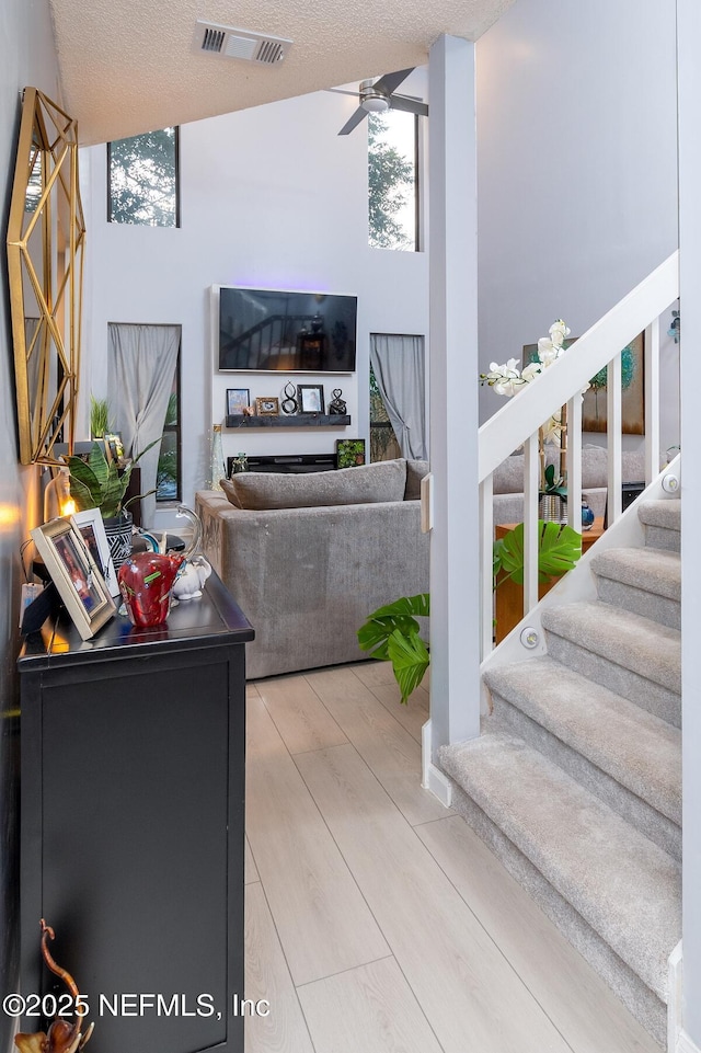 living room featuring visible vents, a ceiling fan, a textured ceiling, wood finished floors, and stairway