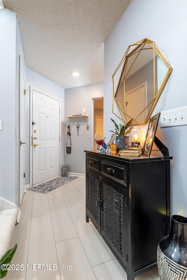 entrance foyer with baseboards, a textured ceiling, and light wood-style floors