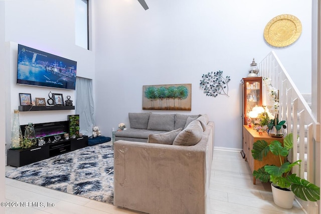 living area with baseboards, wood finished floors, a glass covered fireplace, and a towering ceiling