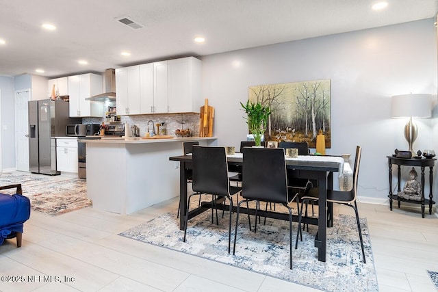 kitchen with visible vents, wall chimney range hood, decorative backsplash, a peninsula, and stainless steel appliances