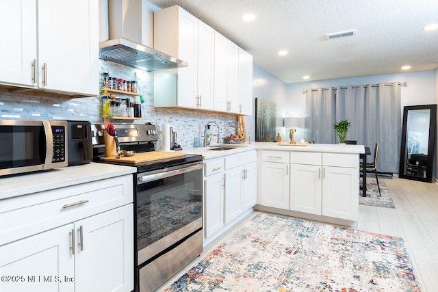 kitchen with visible vents, a sink, a peninsula, appliances with stainless steel finishes, and wall chimney exhaust hood