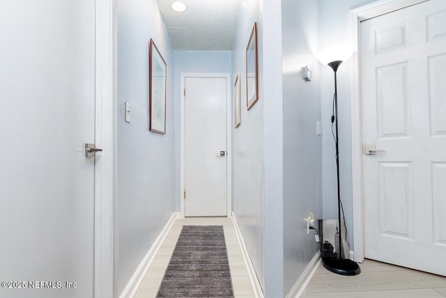 hallway with light wood-type flooring, baseboards, and a textured ceiling