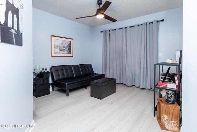 living area featuring ceiling fan, light wood-style flooring, and a textured ceiling