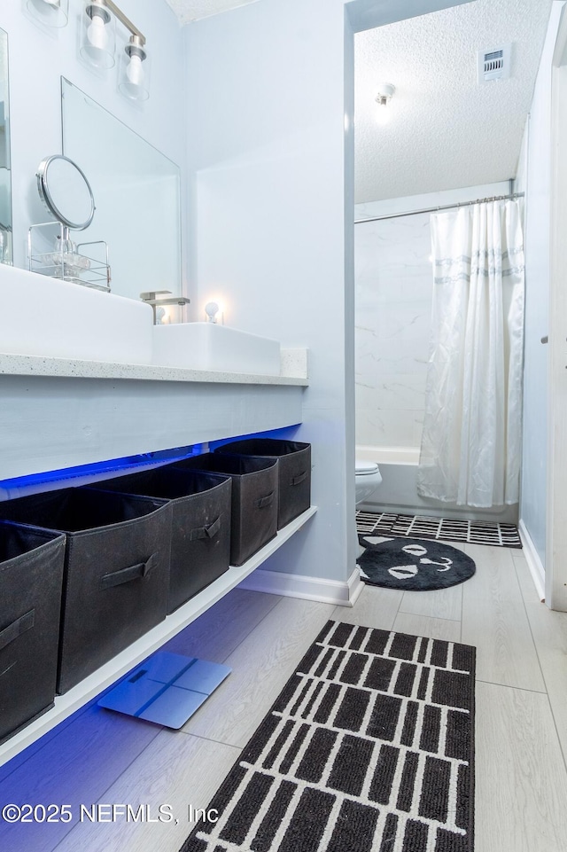 full bathroom featuring visible vents, toilet, vanity, shower / bath combo, and a textured ceiling