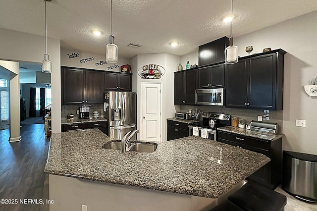 kitchen with a sink, dark stone counters, appliances with stainless steel finishes, and wood finished floors